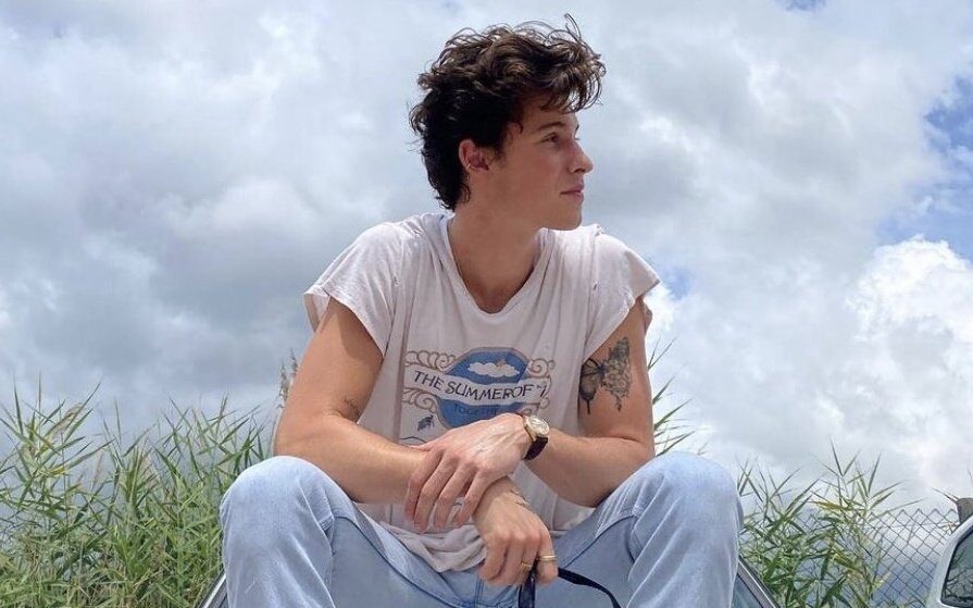 "Summer of Love": Shawn Mendes compartilhou trecho de novo single. Na imagem ele aparece sentado no capô de um carro, olhando para o lado e com nuvens de fundo.